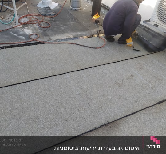 אדם מתקין יריעות איטום על גג עם מבער